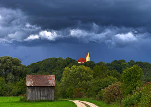 Blick auf die Burger Kirche - schwere Gewitterwolken hängen am Himmel und bevor sich die Sonne geschlagen gibt, taucht sie das Mindeltal in ein besonders stimmungsvolles Licht. (20.9.22)